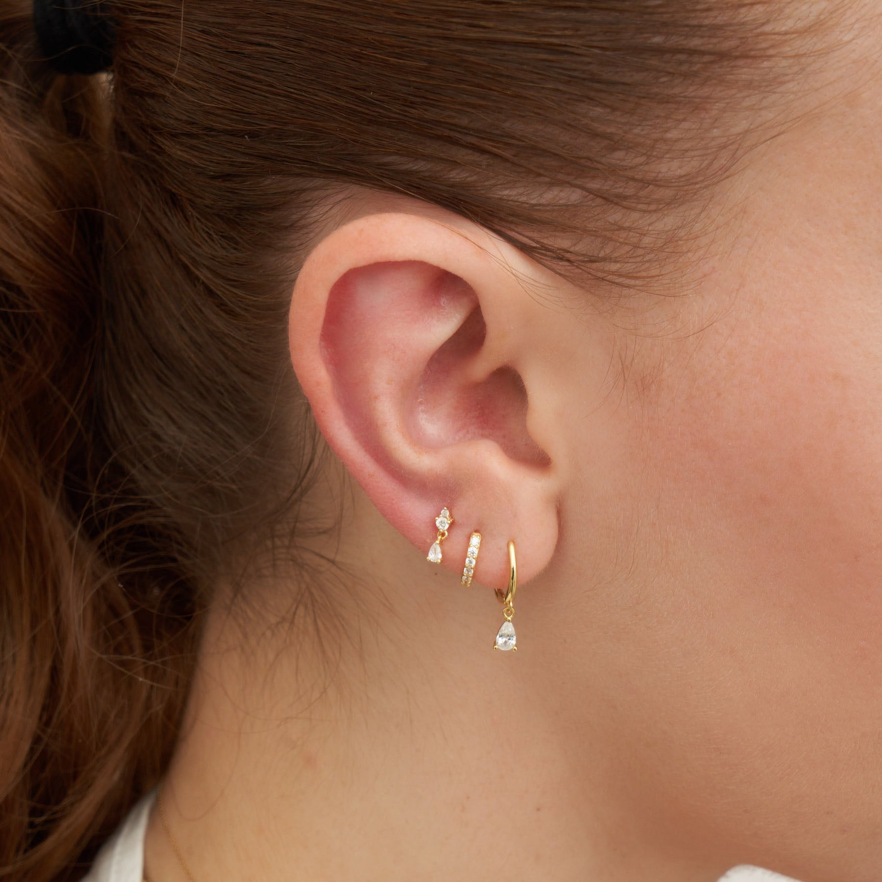 Close-up of an ear wearing gold earrings with a blurred background