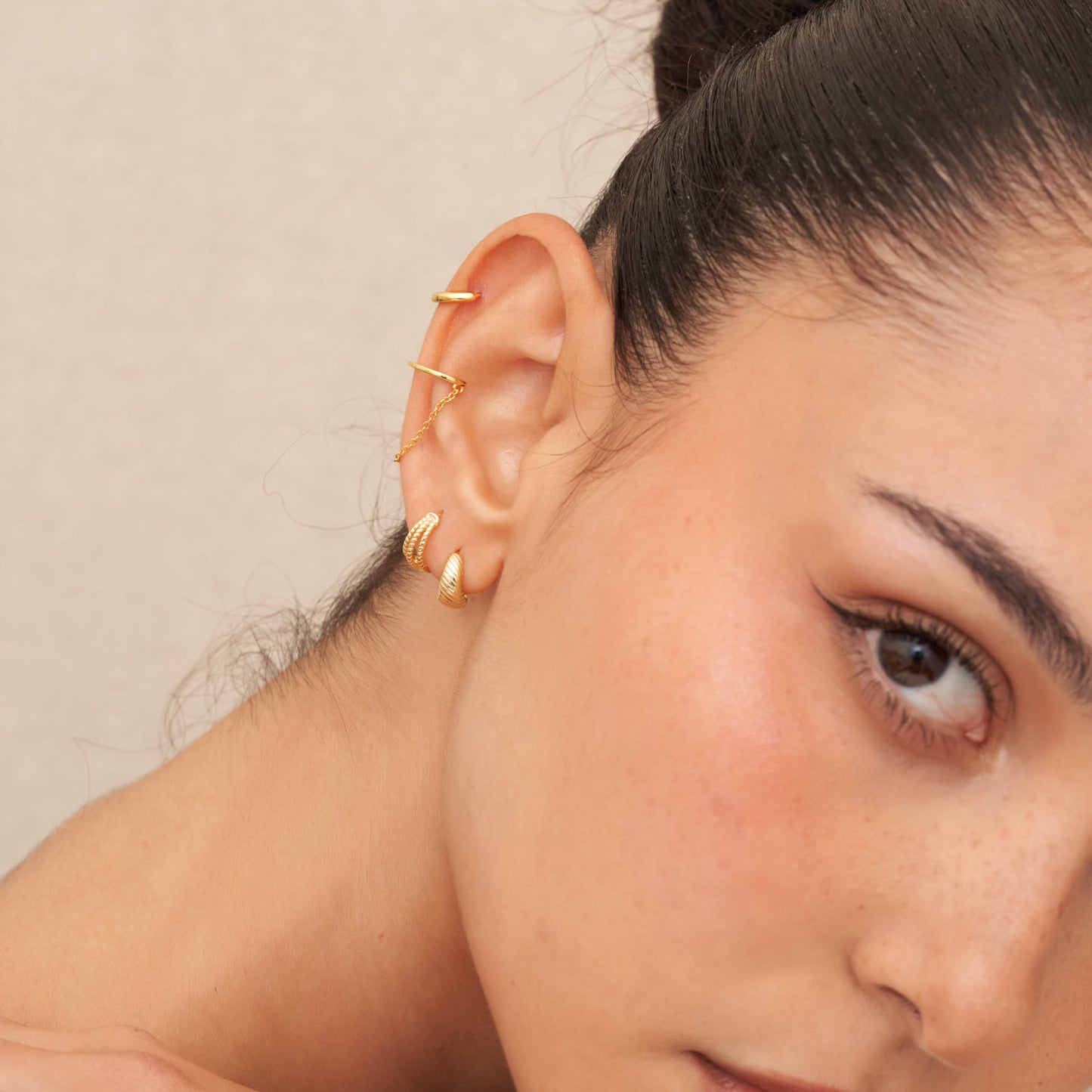 Close-up of a person wearing gold hoop earrings with a neutral background