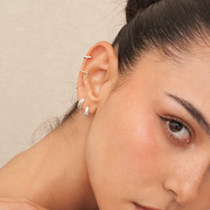 Close-up of a person wearing silver earrings with a neutral background