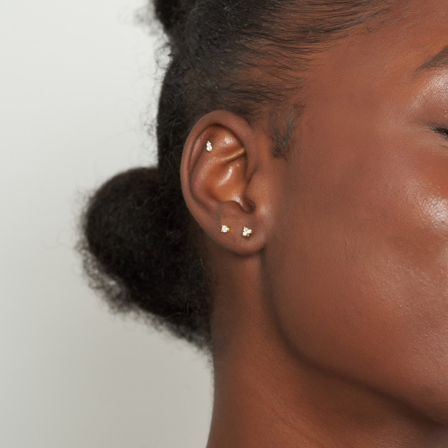 Close-up of an ear with multiple gold earrings against a neutral background