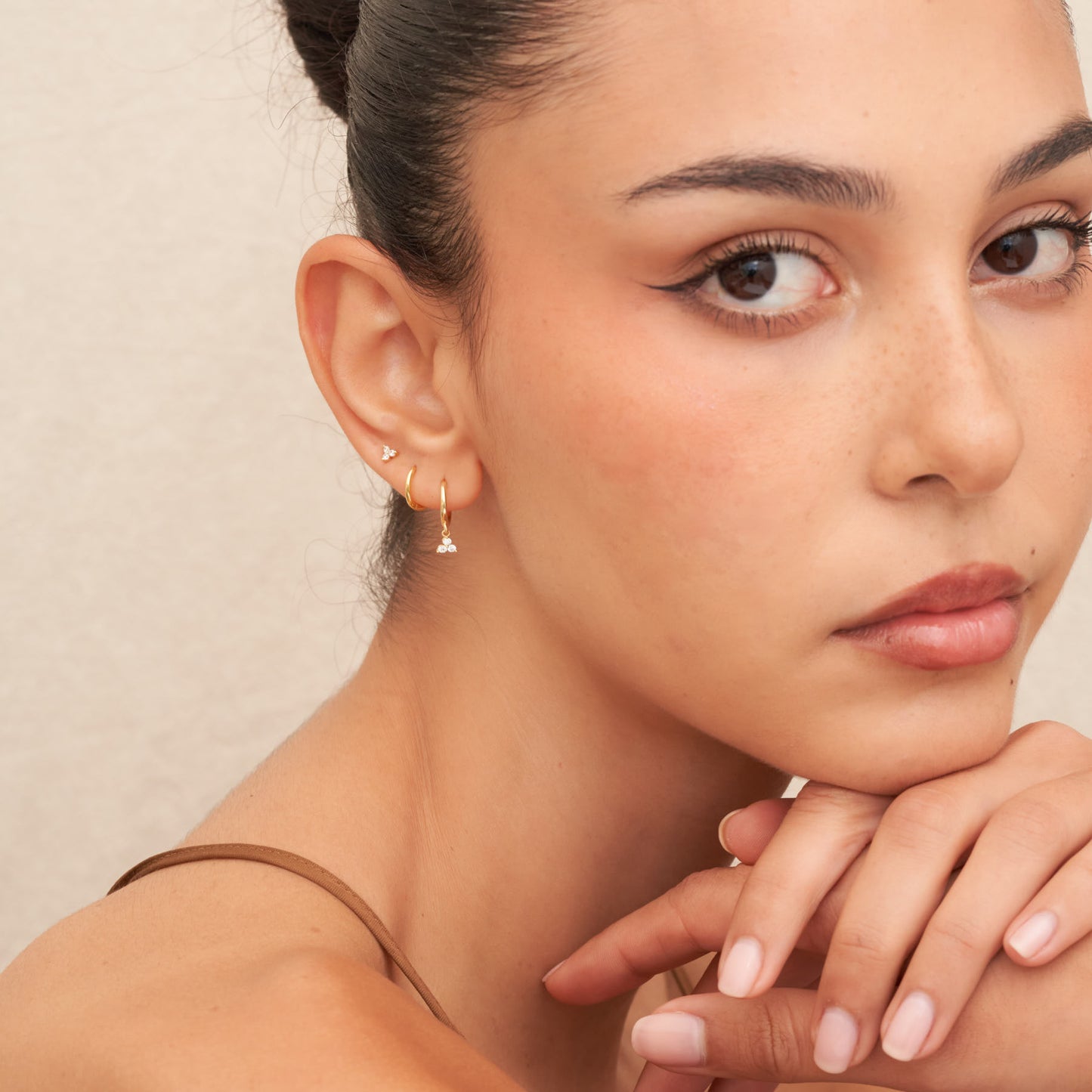 Close-up of a woman wearing gold earrings with a neutral background