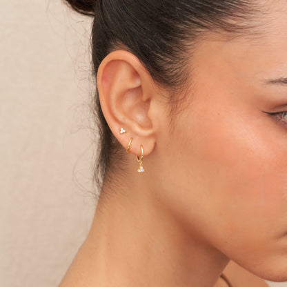 Close-up of a person wearing gold hoop earrings against a neutral background
