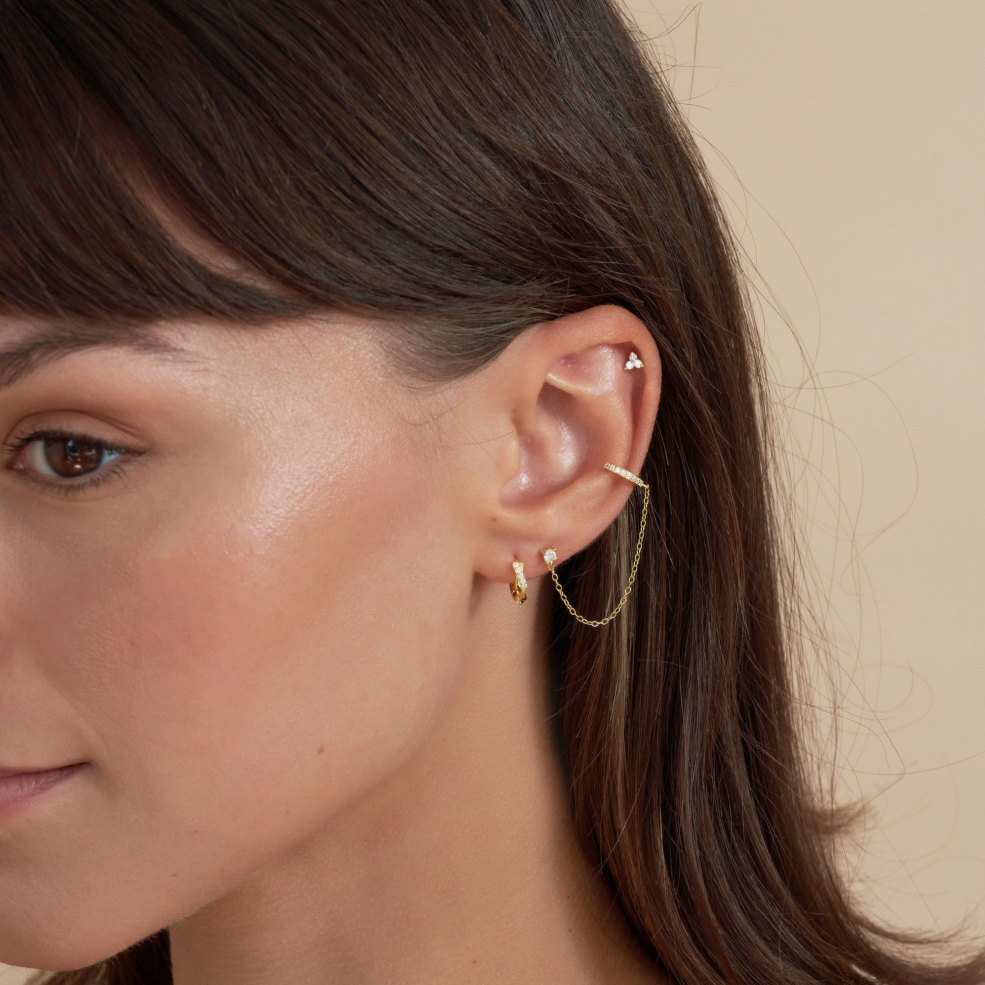 Close-up of a woman's ear wearing gold earrings against a neutral background