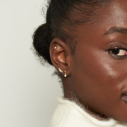 Close-up of a woman's ear with gold earrings against a neutral background