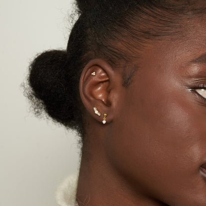 Close-up of a person wearing gold earrings with small pearls against a neutral background