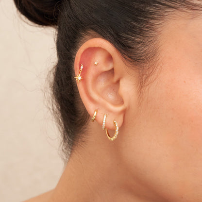 Close-up of an ear with gold earrings on a neutral background