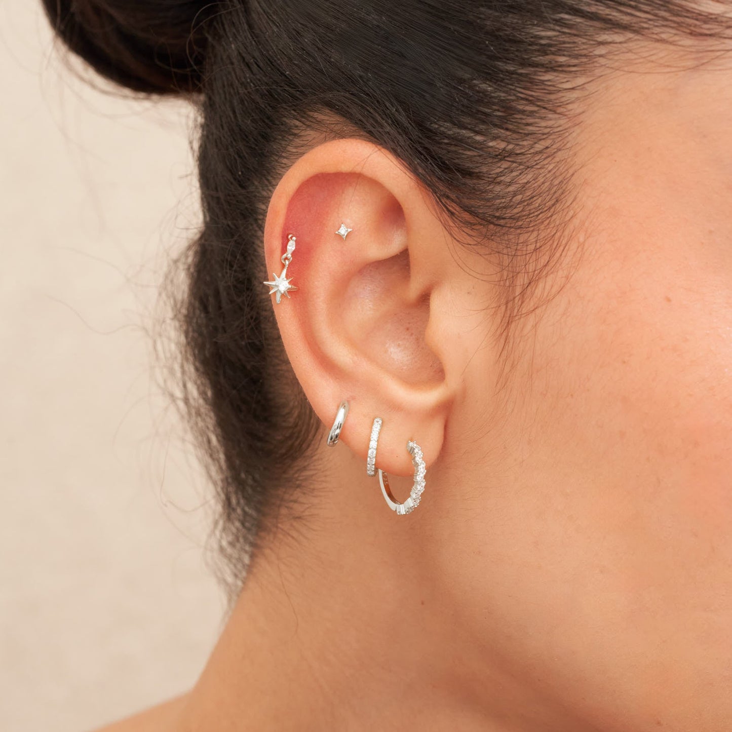 Close-up of an ear with multiple earrings on a neutral background