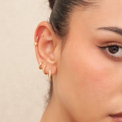 Close-up of an ear with multiple earrings on a neutral background
