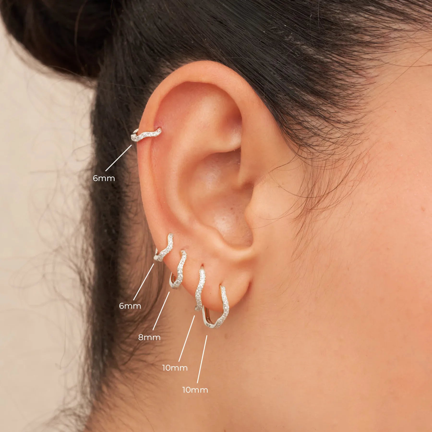 Close-up of an ear wearing silver hoop earrings with size labels.