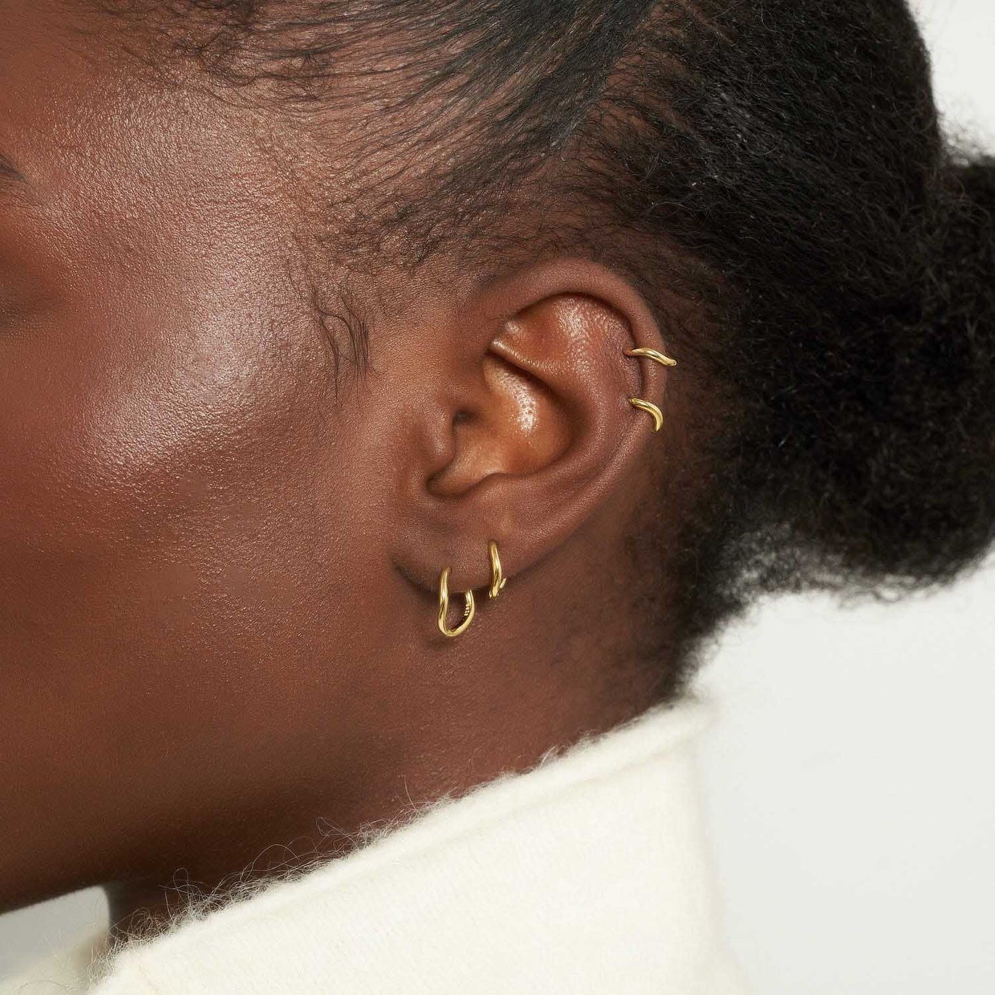 Close-up of an ear with multiple earrings on a neutral background
