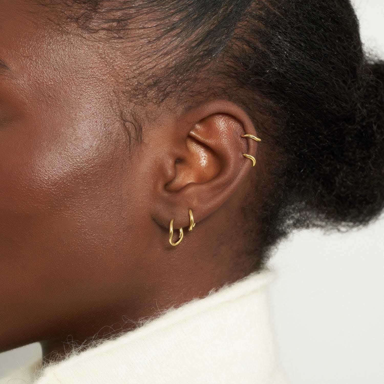Close-up of an ear with multiple earrings on a neutral background