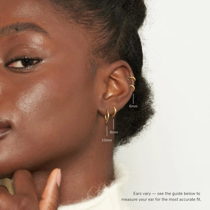 Close-up of a person wearing gold hoop earrings with size measurements on a neutral background.
