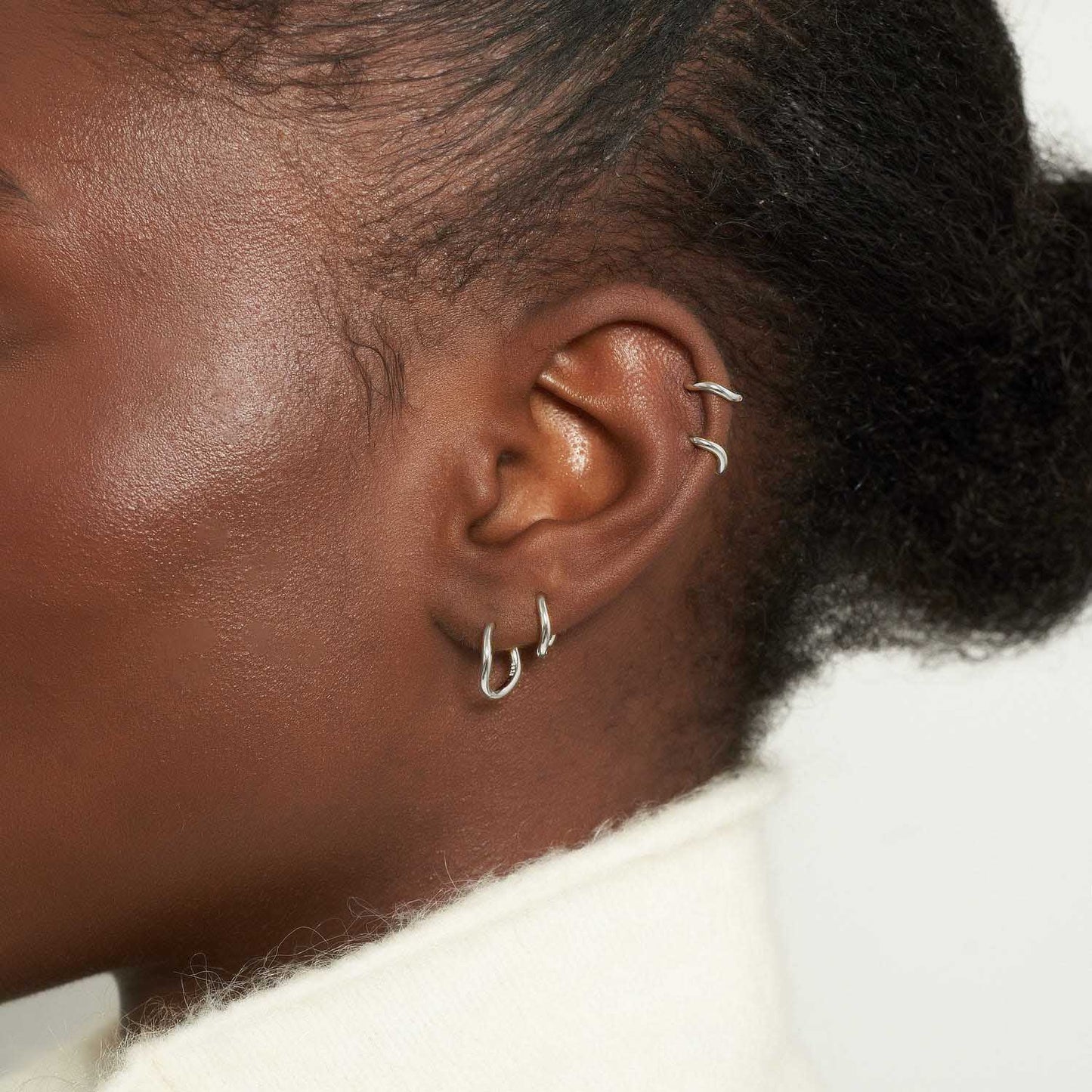 Close-up of an ear with multiple earrings on a neutral background