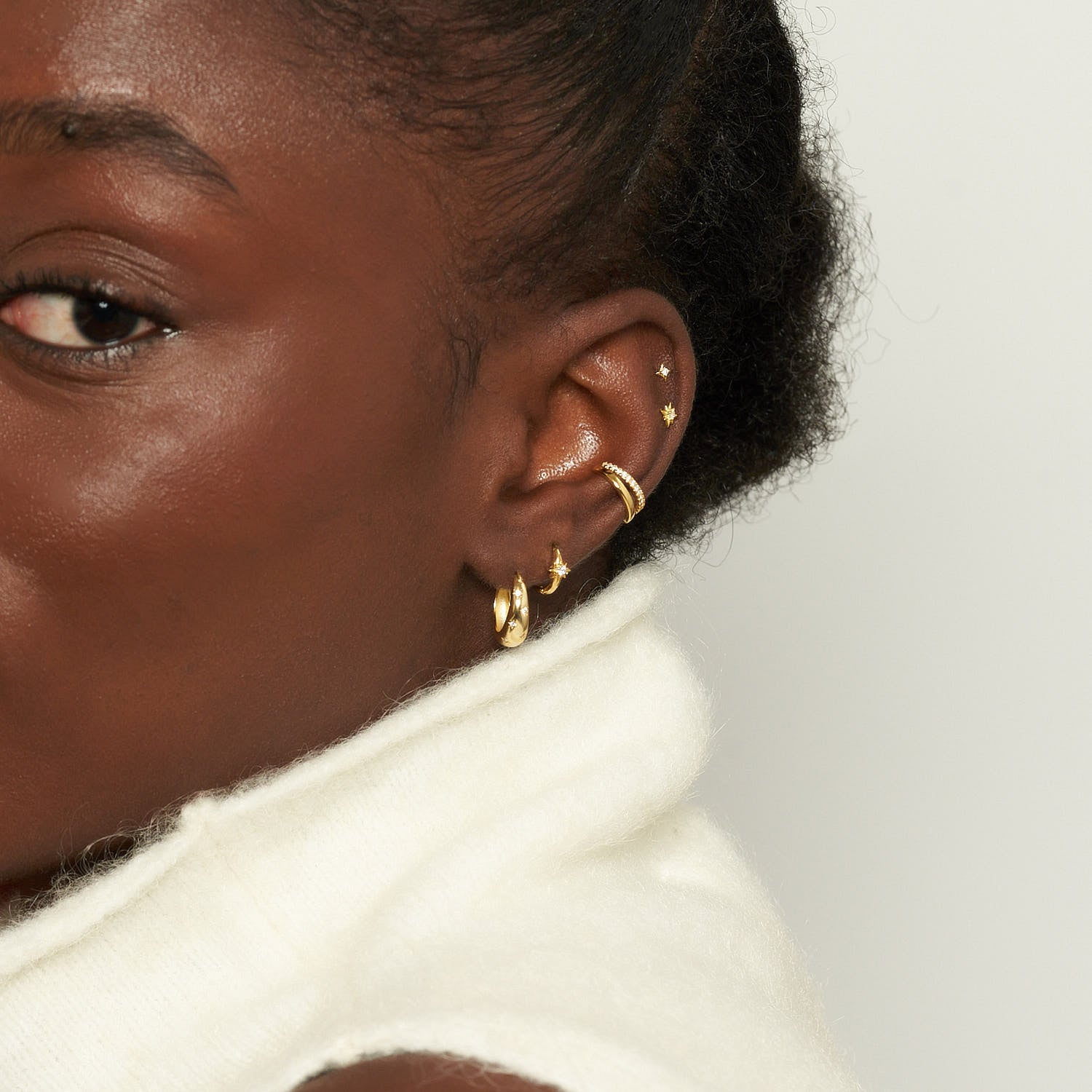 Close-up of an ear with gold earrings on a neutral background