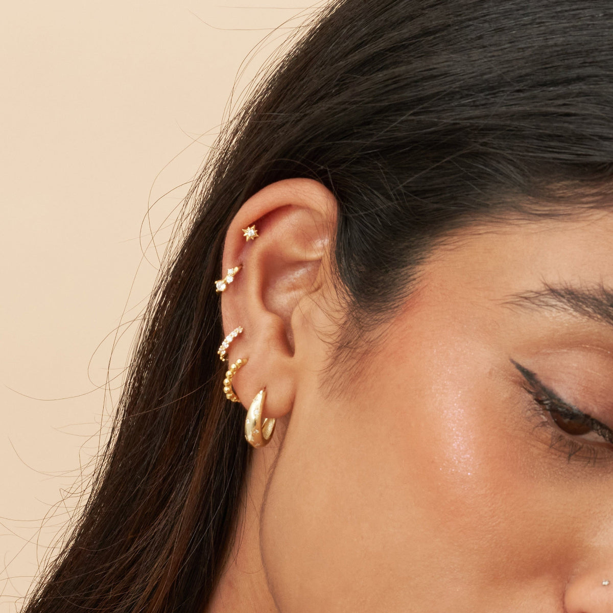 Close-up of a woman's ear with gold earrings against a beige background