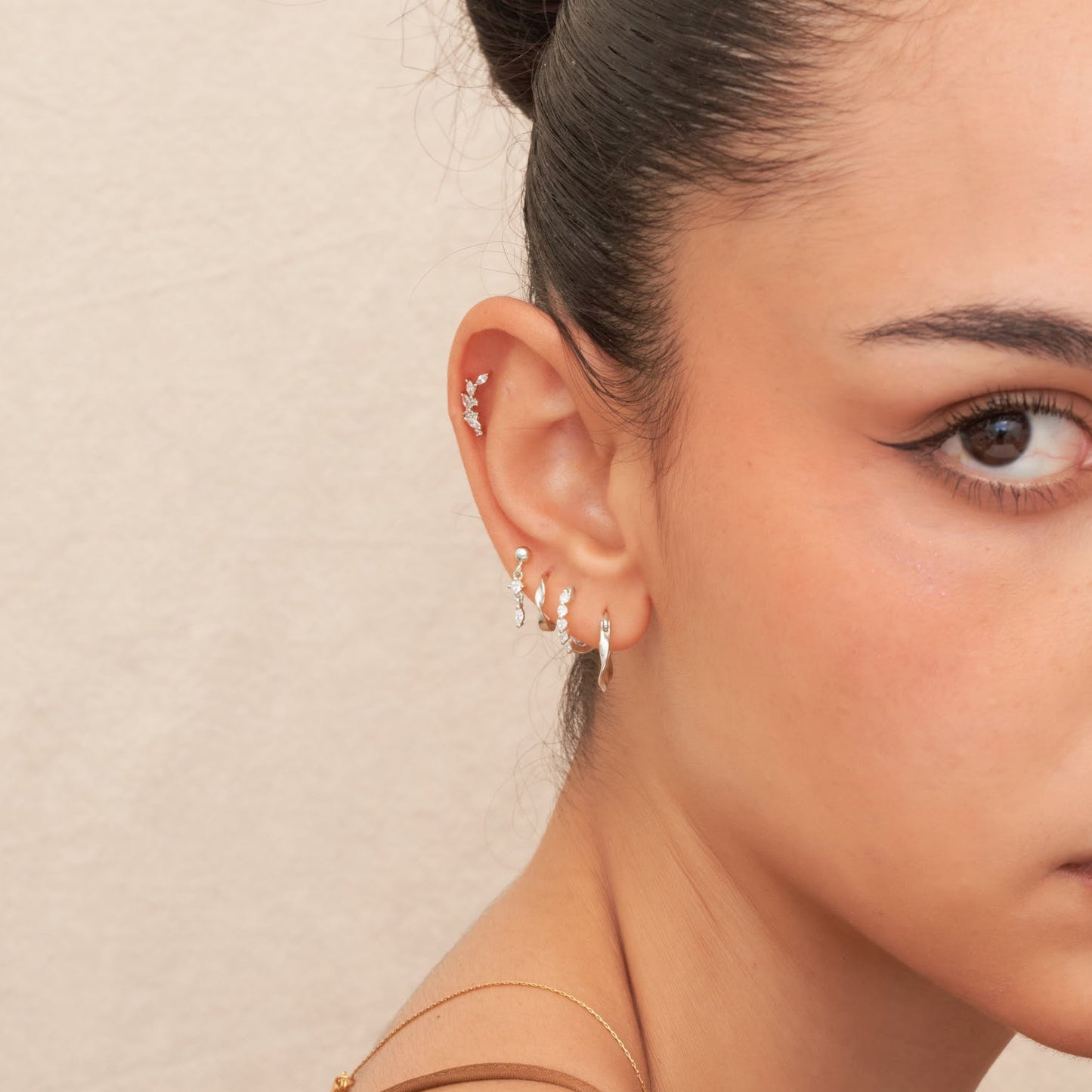 Close-up of a woman's ear with multiple earrings against a neutral background