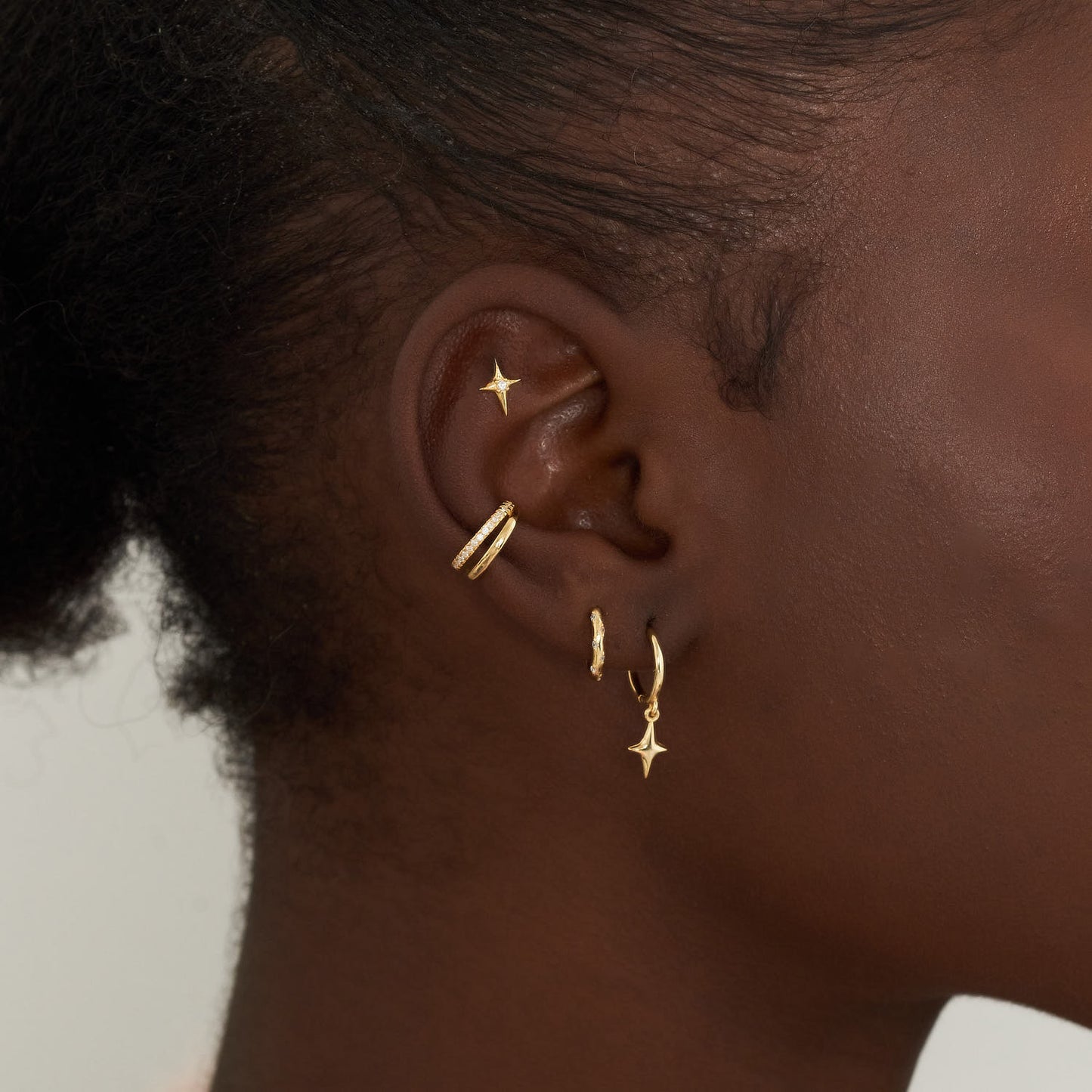 Close-up of an ear wearing gold hoop earrings with star-shaped ends.