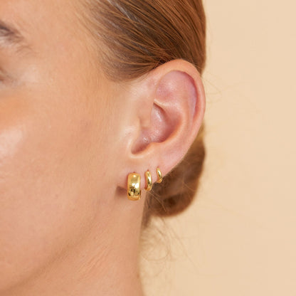 Gold hoop earrings worn by a person on a beige background