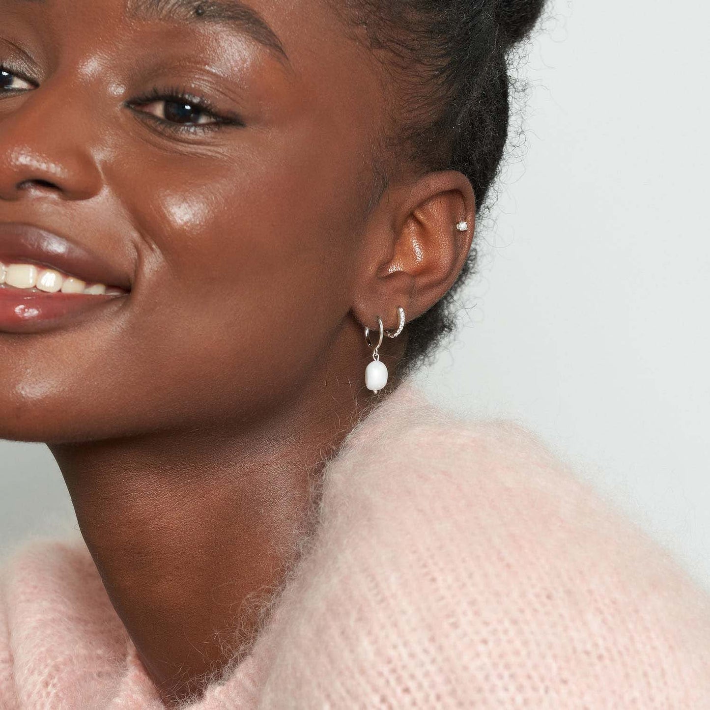 Close-up of a woman wearing pearl earrings with a light pink sweater.