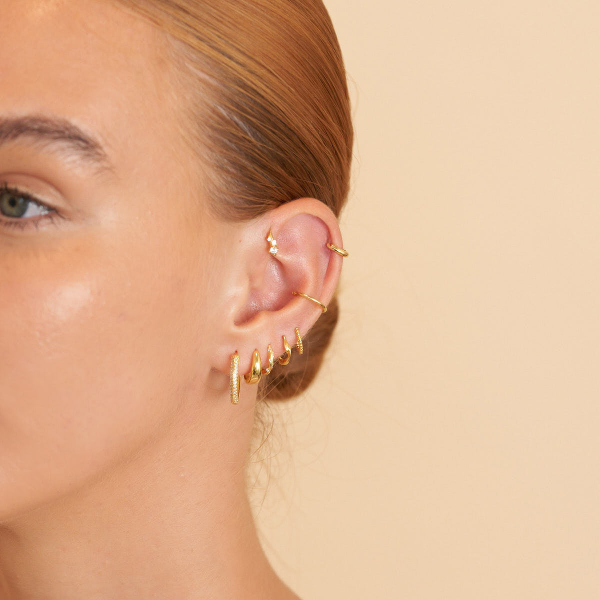 Close-up of a person's ear with gold earrings on a beige background