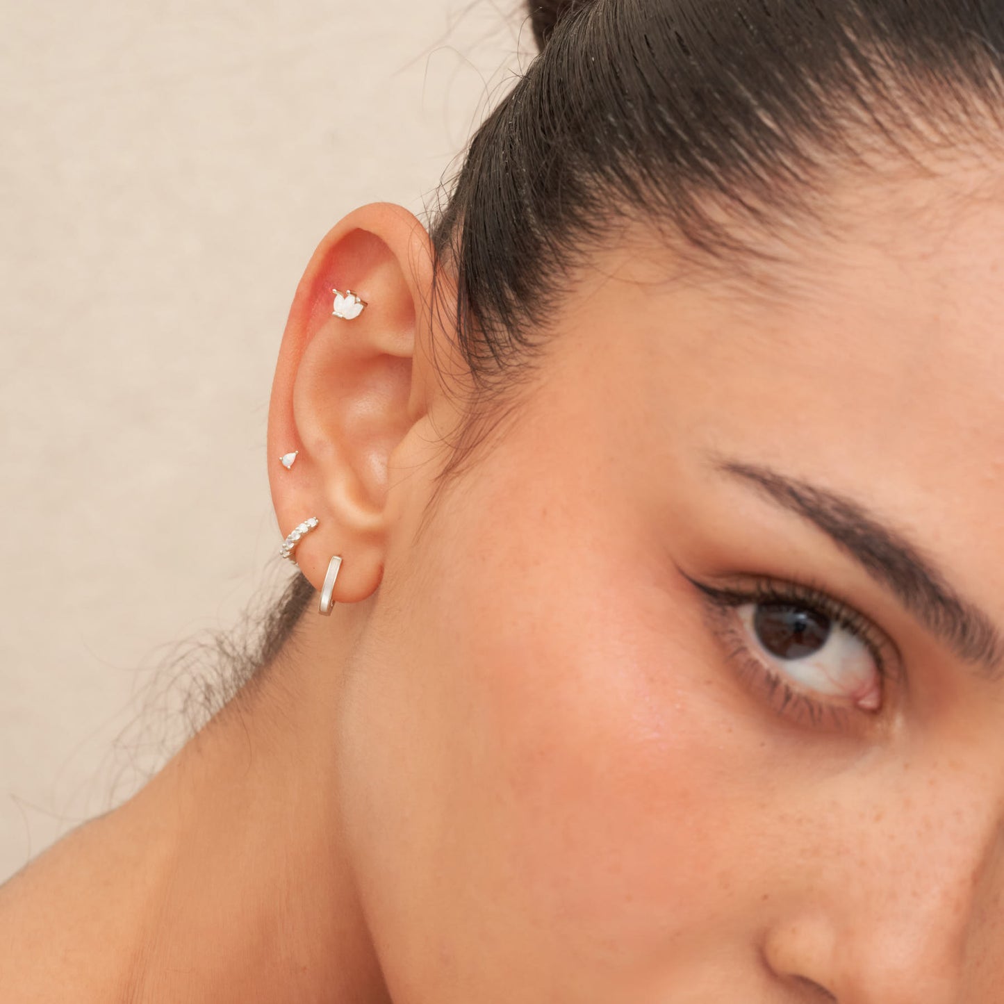 Close-up of a person wearing multiple earrings with a neutral background