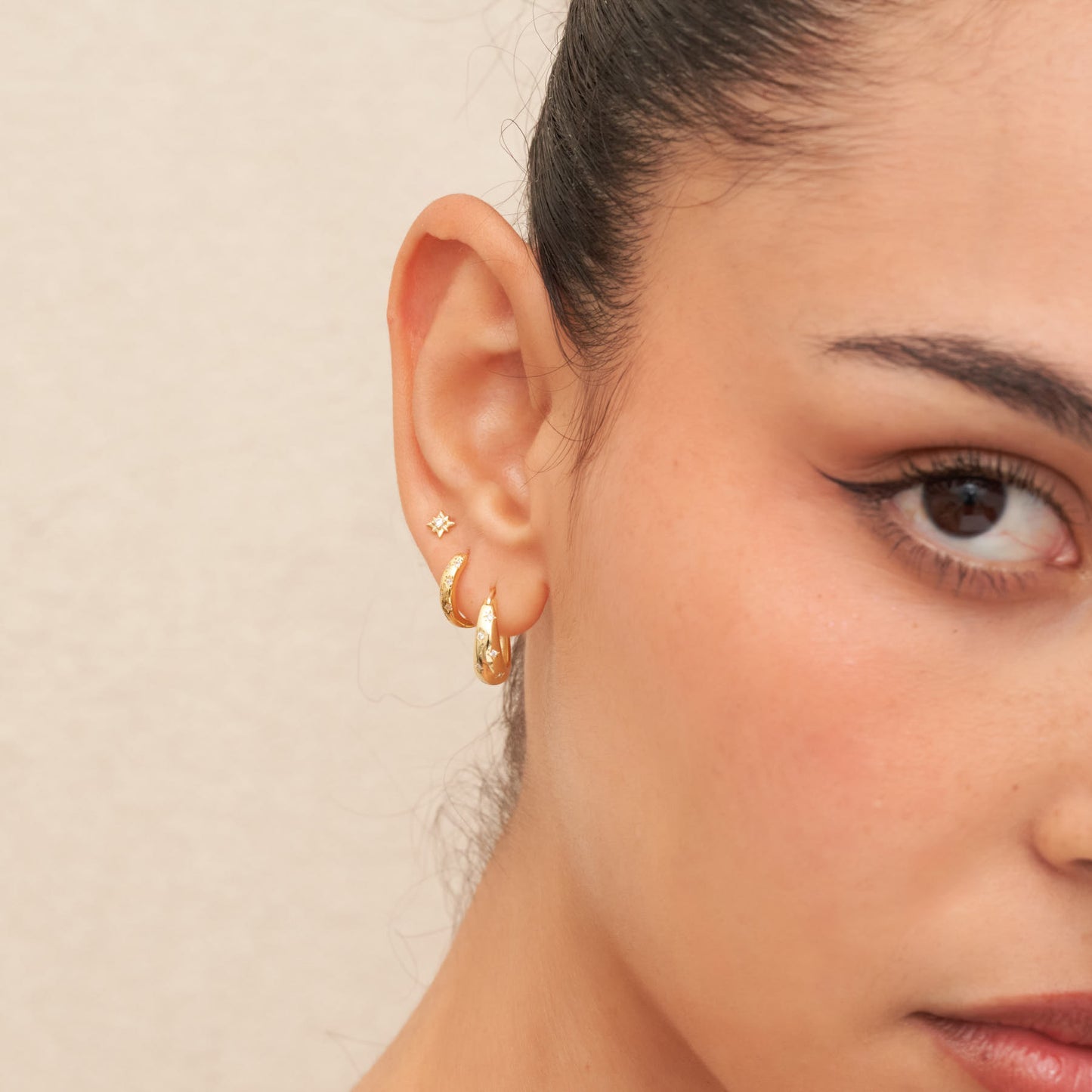 Close-up of a person wearing gold hoop earrings with a neutral background