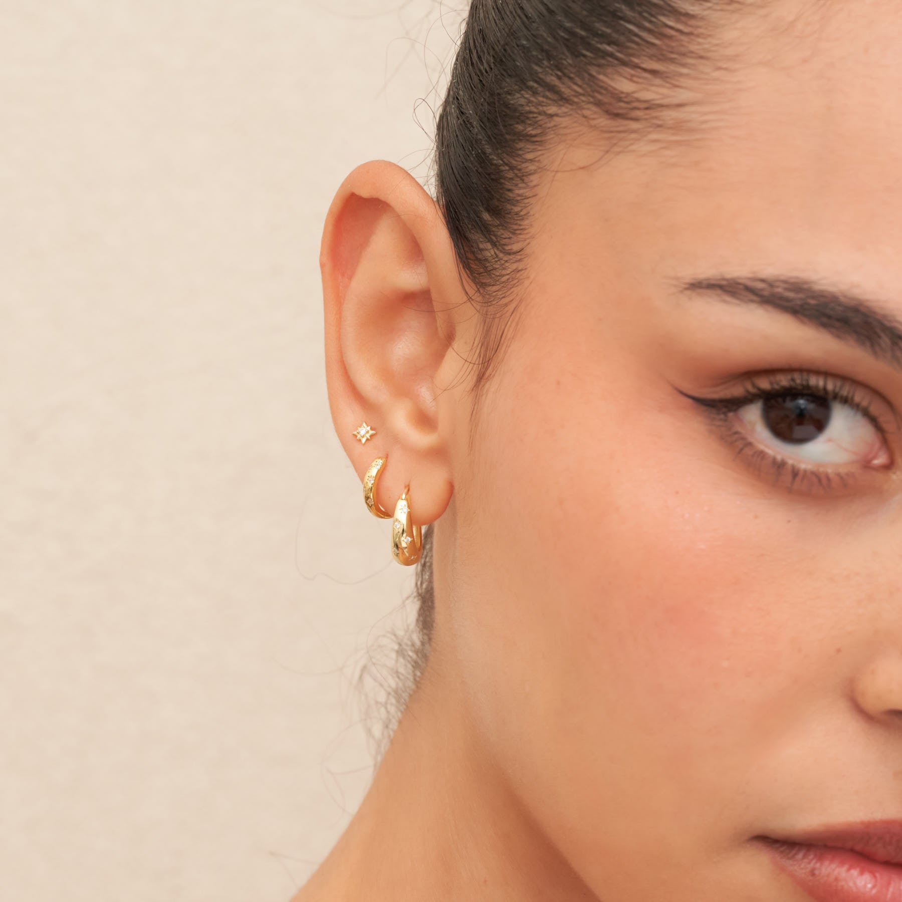 Close-up of a person wearing gold hoop earrings with a neutral background