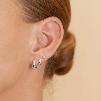 Close-up of an ear wearing silver hoop earrings on a beige background